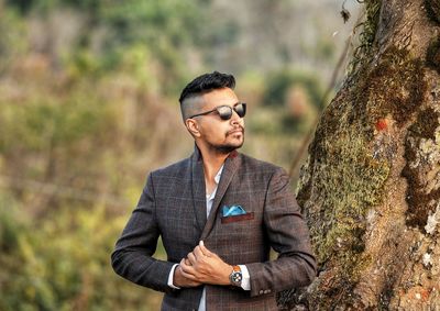 Young man looking away while standing on tree trunk