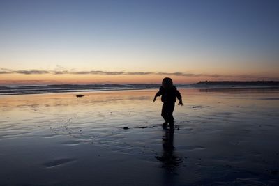 Silhouette woman standing on beach against sky during sunset