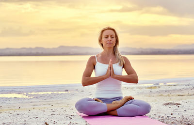 Woman doing yoga at beach during sunrise