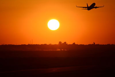 Silhouette airplane flying against orange sky