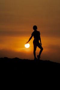 Silhouette man standing on field against orange sky