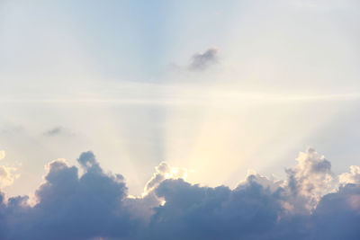 Low angle view of sunlight streaming through clouds