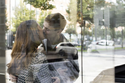 Young couple kissing seen through glass window of real estate office
