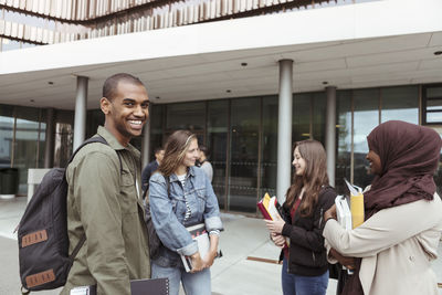 Portrait of smiling man standing with female friends talking at campus in university