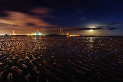 Illuminated beach against sky at night