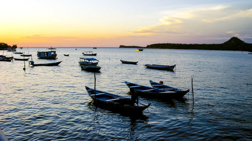 Boats moored in sea against sky during sunset