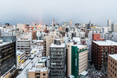 High angle view of city buildings during winter season against cloudy sky