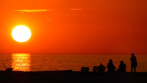 Silhouette people standing on beach against orange sky