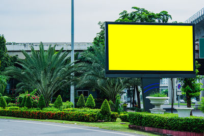 Yellow road sign by trees against sky in city