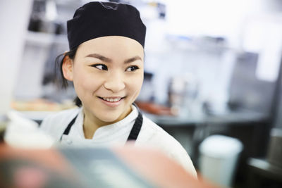 Smiling female chef looking away in commercial kitchen