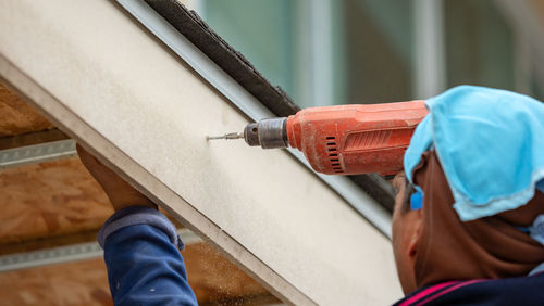 Close-up of manual worker drilling roof at construction site