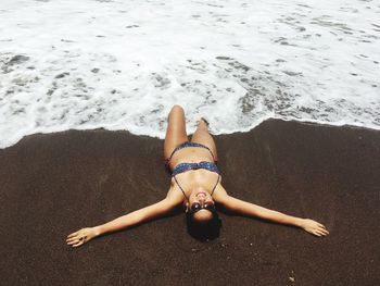 High angle view of woman in bikini lying on sea shore at beach