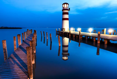 Wooden posts in sea against sky at dusk