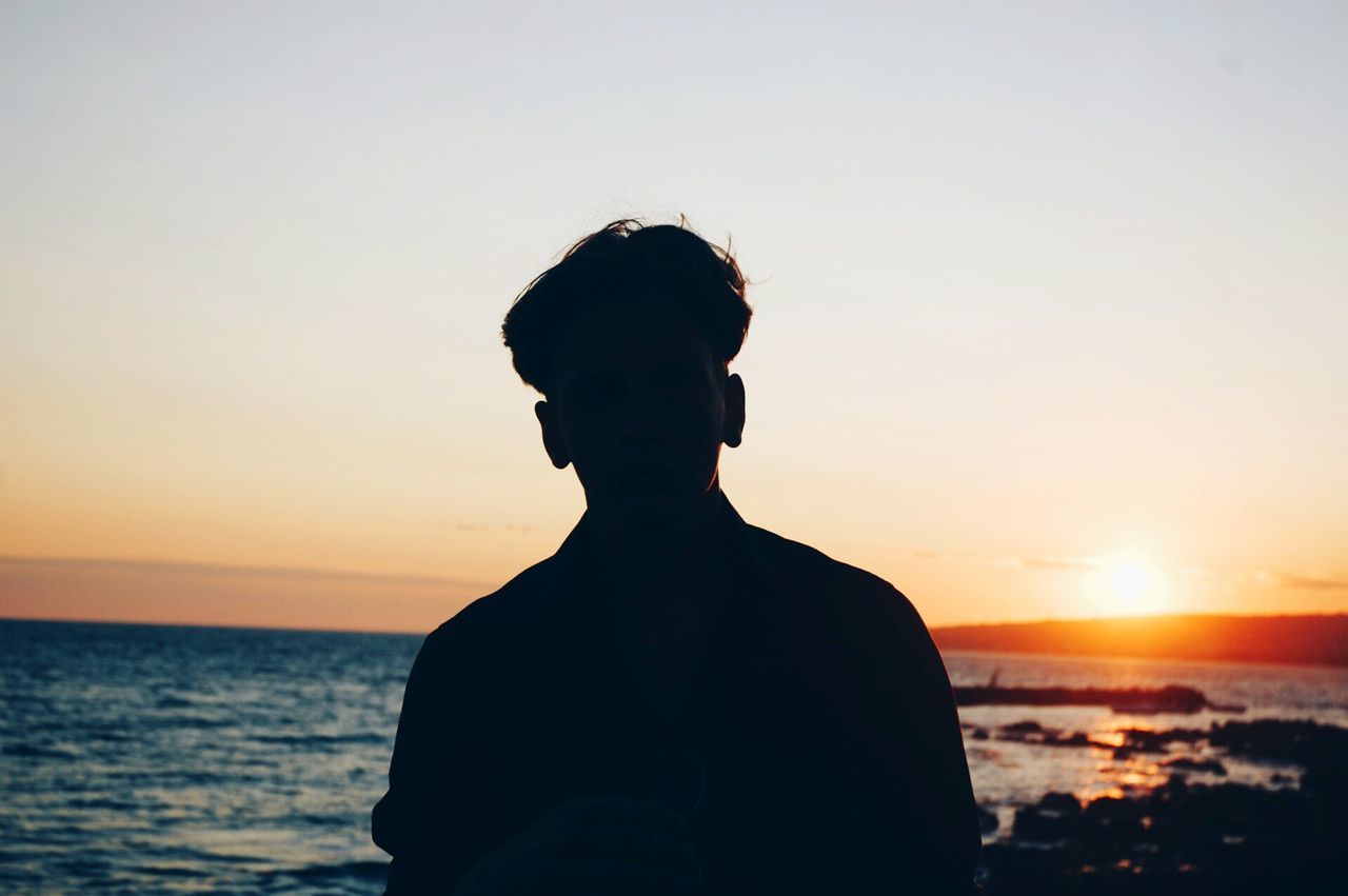 sunset, sea, horizon over water, lifestyles, water, standing, waist up, leisure activity, scenics, beauty in nature, orange color, sun, silhouette, rear view, tranquility, three quarter length, sky, tranquil scene