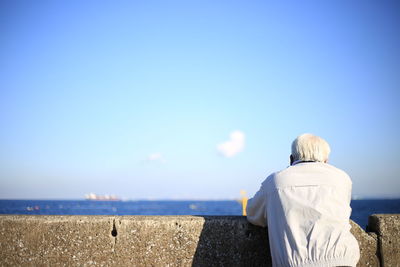 Rear view of woman standing at beach against clear blue sky