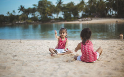 Sisters playing with sand on riverbank against trees