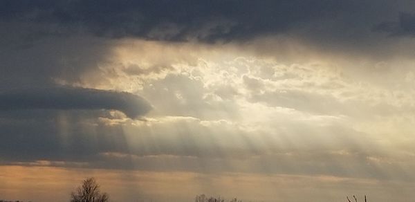 Low angle view of sunlight streaming through clouds