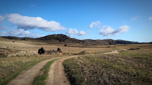 Dirt road on field against sky