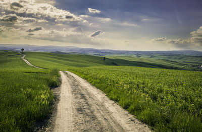 Dirt road amidst field against sky