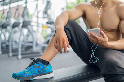 Low section of shirtless muscular man using mobile phone in gym