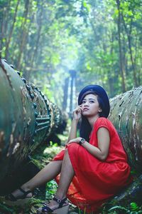Young woman looking away while sitting amidst pipes in forest
