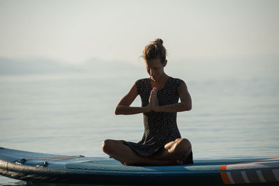 Full length of woman meditating while sitting on paddleboard over lake