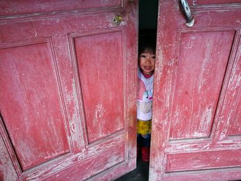Portrait of smiling girl standing behind red door