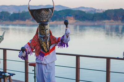 Rear view of person standing by railing against lake