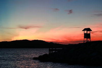 Silhouette built structure by sea against orange sky