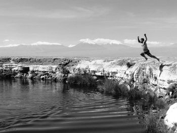 Scenic view of  man jumping in lake with mountains in background