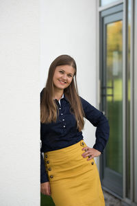 Portrait of smiling young woman standing against wall