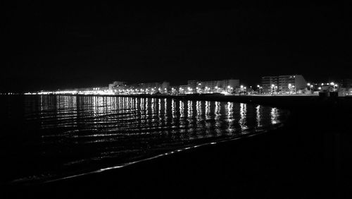 Illuminated buildings by river against sky at night