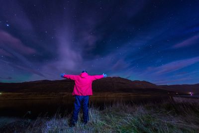 Rear view of man standing on field against sky at night