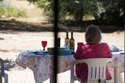 Rear view of woman sitting at table outdoors