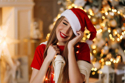 A beautiful young woman in a red santa hat celebrates christmas in a decorated room at home