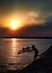 Silhouette man by sea against sky during sunset
