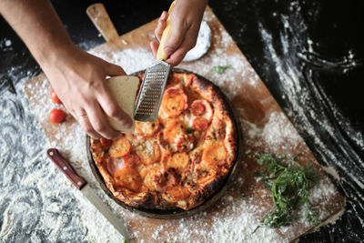 Male hands rubbed cheese grated on pizza, pizza cooking in a real home interior lifestyle and toning