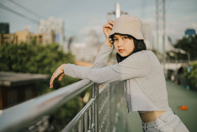 Side view of young woman standing against railing in city