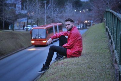 Side view portrait of man sitting at roadside in city during sunset