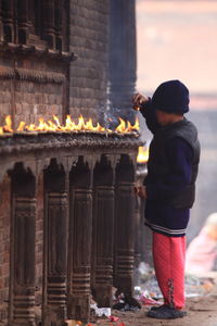 Side view of boy igniting candle at temple