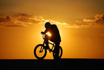 Silhouette man bicycle against orange sky
