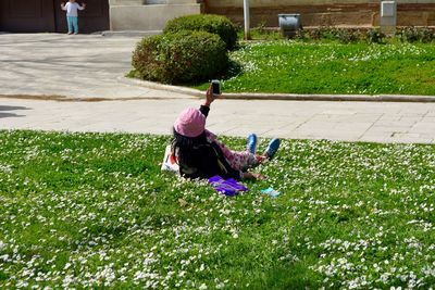 Mid adult woman taking selfie with mobile phone while lying on grassy field at park