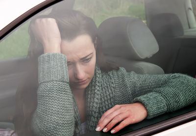 Tensed woman sitting in car seen through window