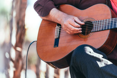 Midsection of man playing guitar while sitting outdoors