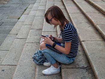 Full length of teenage girl using mobile phone while sitting outdoors