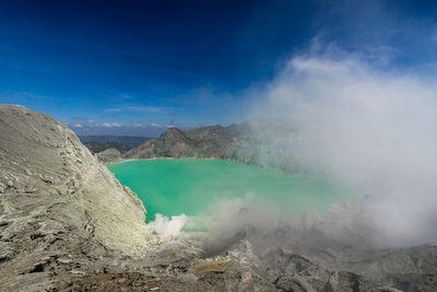 Smoke emitting from volcanic mountain against blue sky