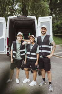 Portrait of smiling male and female coworkers standing against delivery van