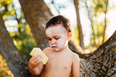 Close-up of shirtless boy holding tree trunk