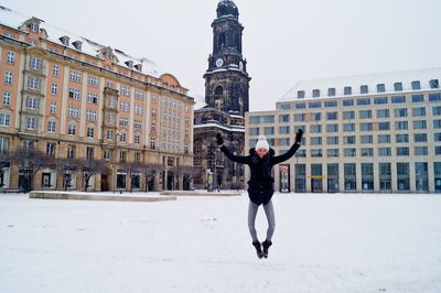 Young woman in mid-air over snow covered field against kreuzkirche