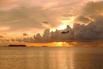 Low angle view of airplane flying over sea during sunset